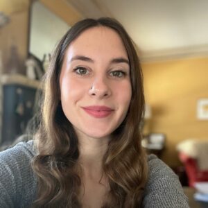 Emma Joswiak-McLaughlin smiles at the camera in a living room. She has brown eyes and a kind face.